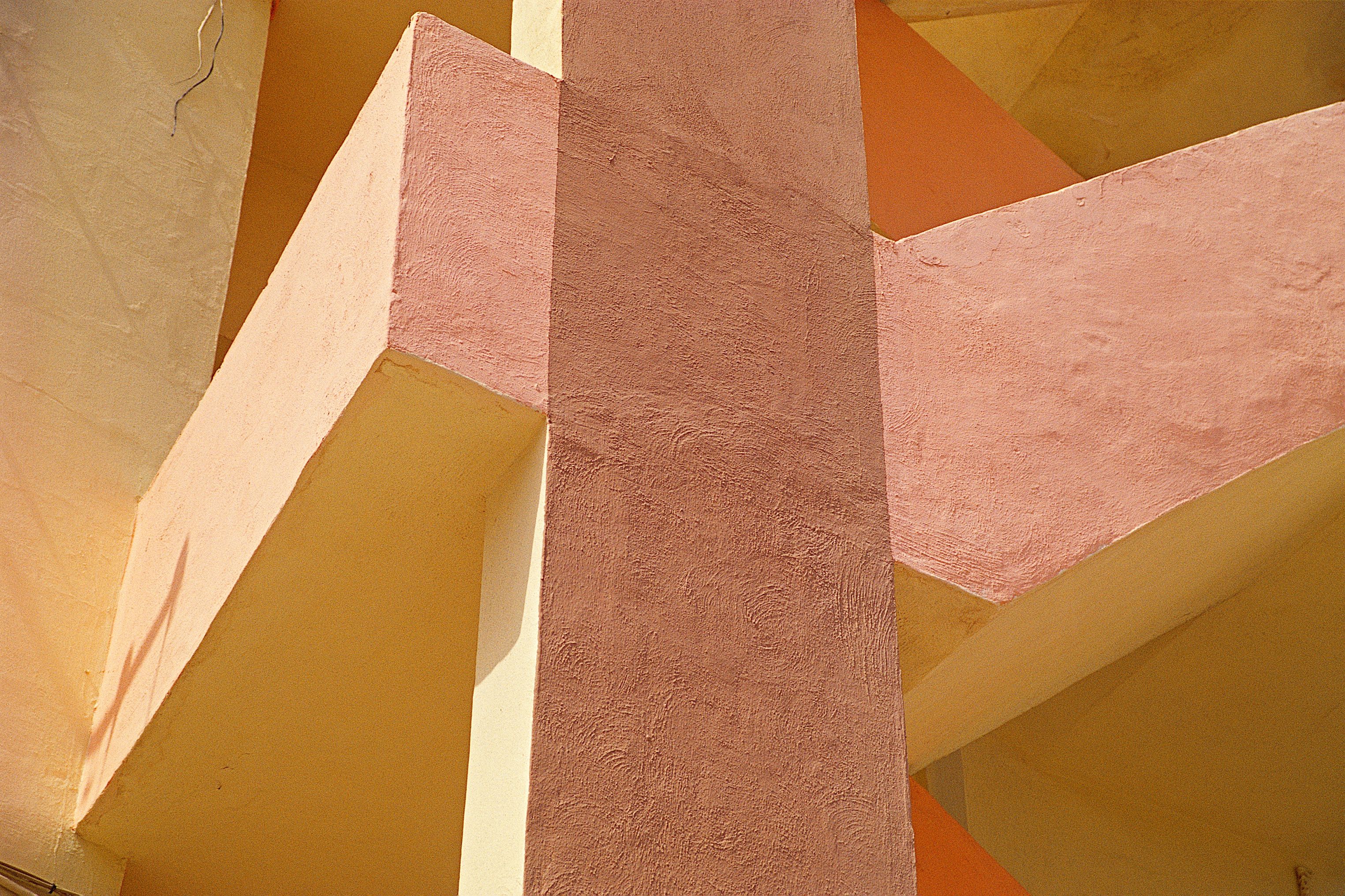 Architekturdetail aus rosa, apricot und gelb getönten Betonflächen, deren Pfeiler und Träger sich überschneiden