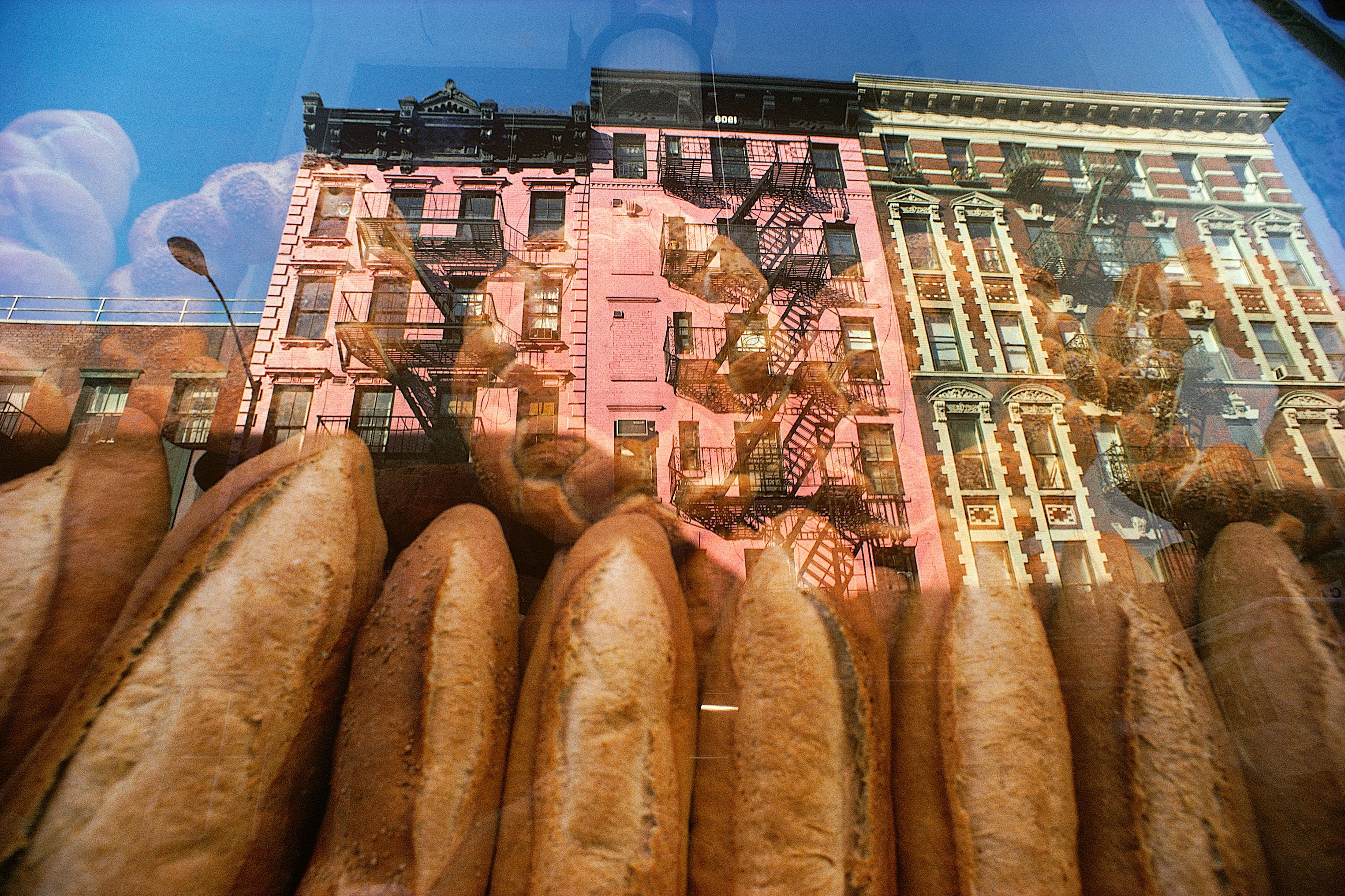 Baguettes im Schaufenster einer Bäckerei, in der Scheibe spiegeln sich Häuserfassaden mit Feuerleitern